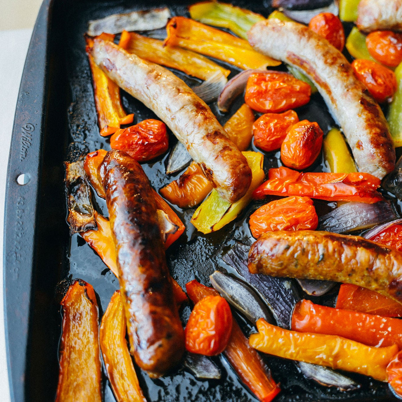 Roasted sausages and vegetables on a baking tray