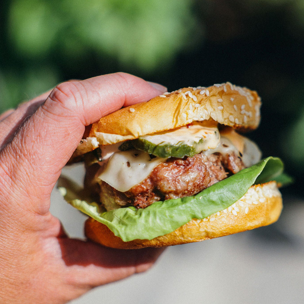 Hand holding a burger with lettuce and cheese against a blurred green background