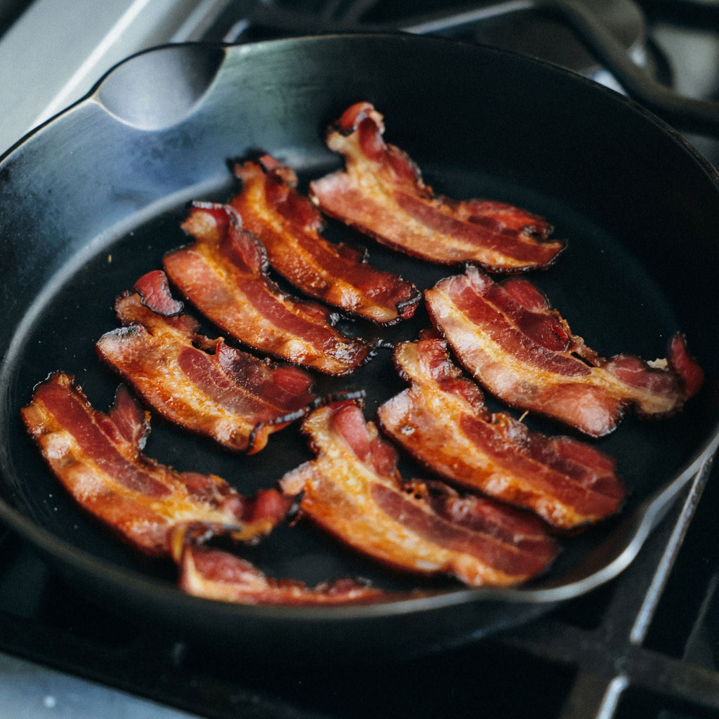 Bacon cooking in a cast iron frying pan on a stovetop