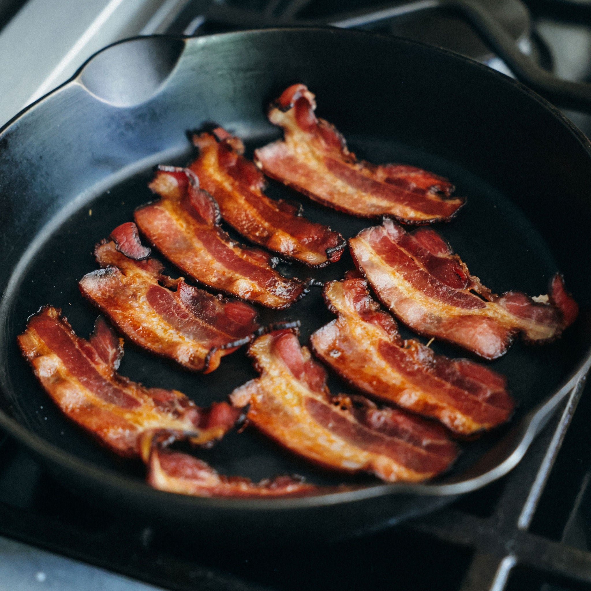 Bacon cooking in a cast iron frying pan on a stovetop