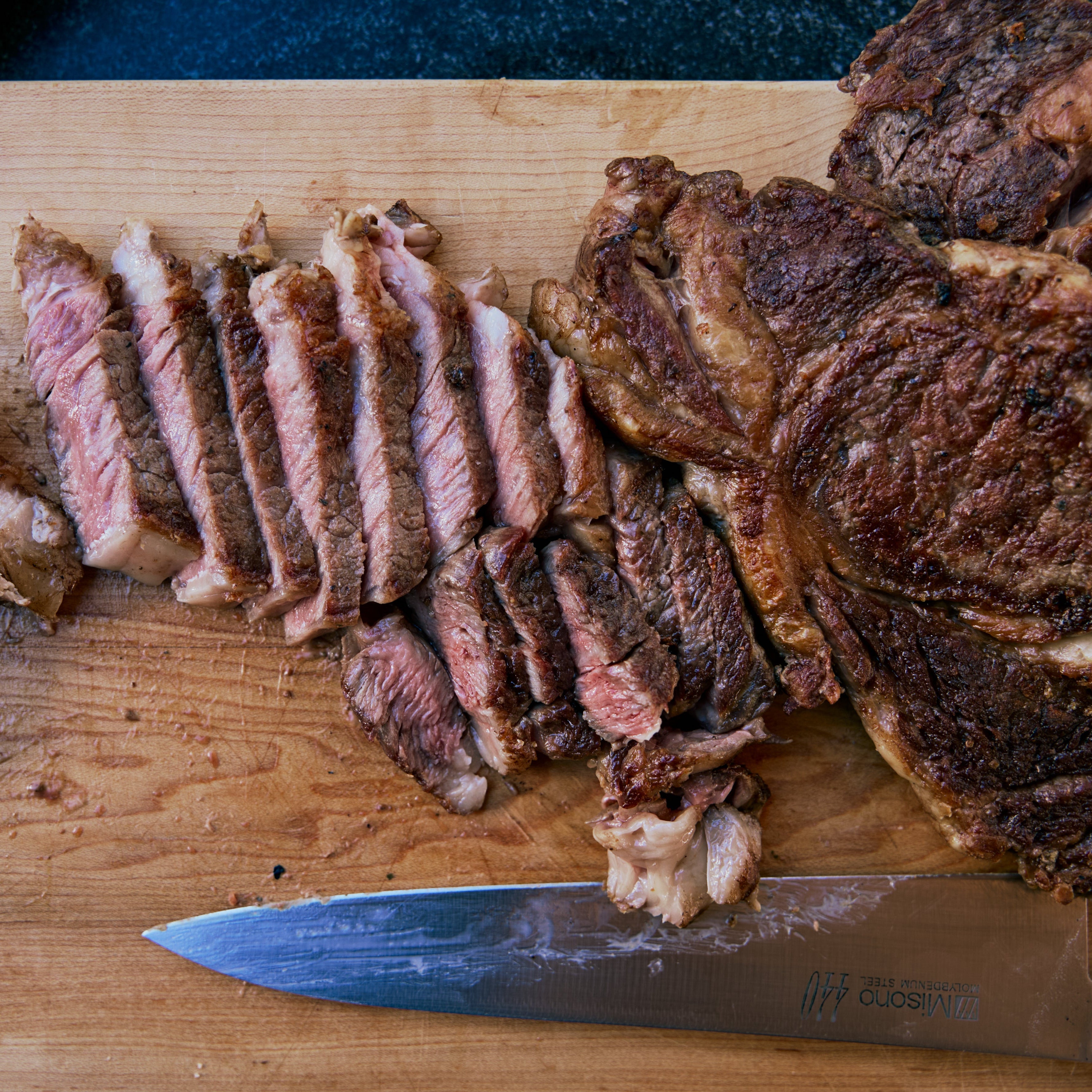 Sliced grass-fed ribeye steak on a wooden cutting board with a knife