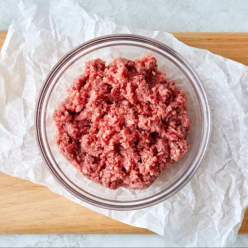 Glass bowl with ground meat on a white paper background