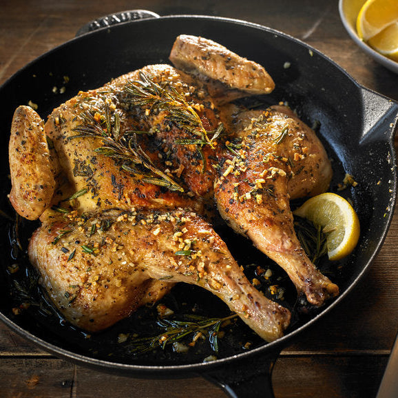 Roasted chicken with lemon wedges in a cast iron skillet on a wooden surface